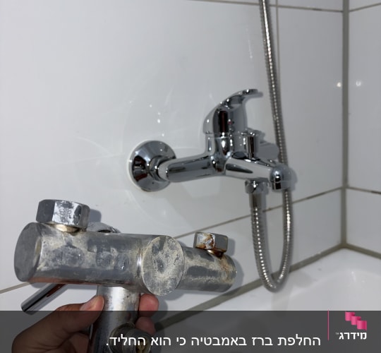 ברז אמבטיה מוחזק ביד ליד קיר אריחים